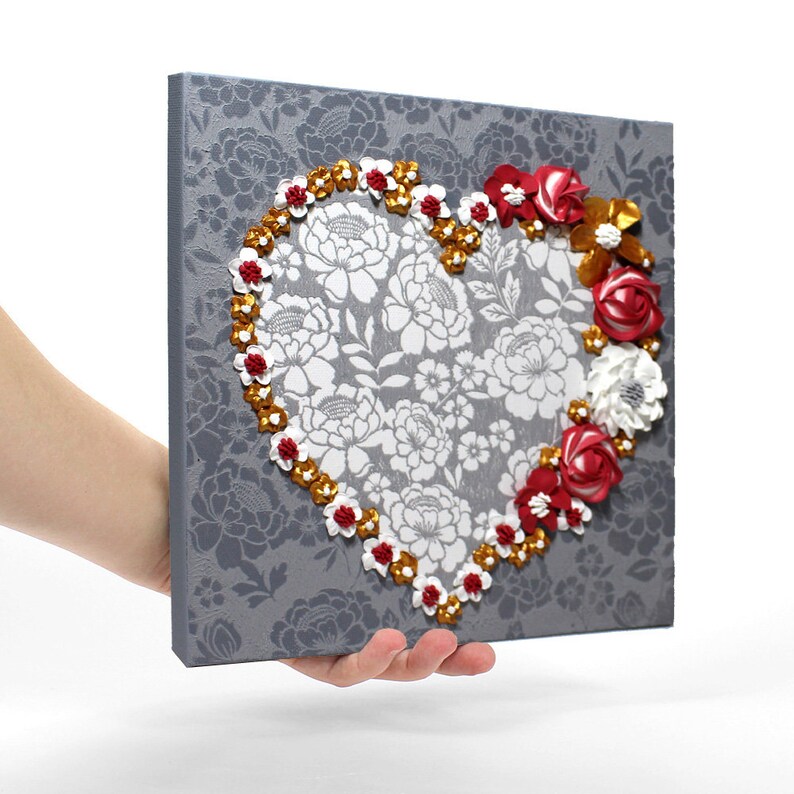 Held in hand angled view of painting of heart art in red and gold with sculpted rose floral artwork on small canvas