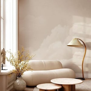 May include: A beige living room with a cream sofa, two round coffee tables with wooden bases, and a floor lamp with a pleated shade. A vase of yellow branches sits by the window, adding a natural element to the space.