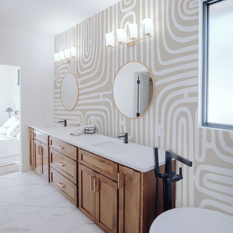 May include: A modern bathroom with a wooden vanity, white countertop, and black fixtures. The room features two round mirrors and a patterned wallpaper in beige and white. Overhead, there are two sets of light fixtures.