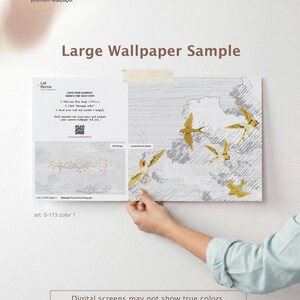May include: A large wallpaper sample featuring a design of gold birds in flight against a gray and white background. The sample is held up, showcasing the design and the text "Large Wallpaper Sample". The brand name "Lilii Borea" is visible.
