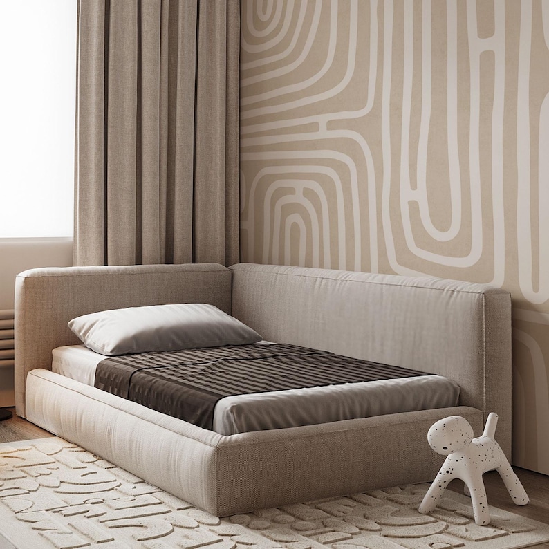 May include: A beige upholstered bed with a brown and gray striped blanket and a white pillow. The bed is in a corner of a room with beige curtains and a patterned wall. A white dog-shaped figurine is on the floor.