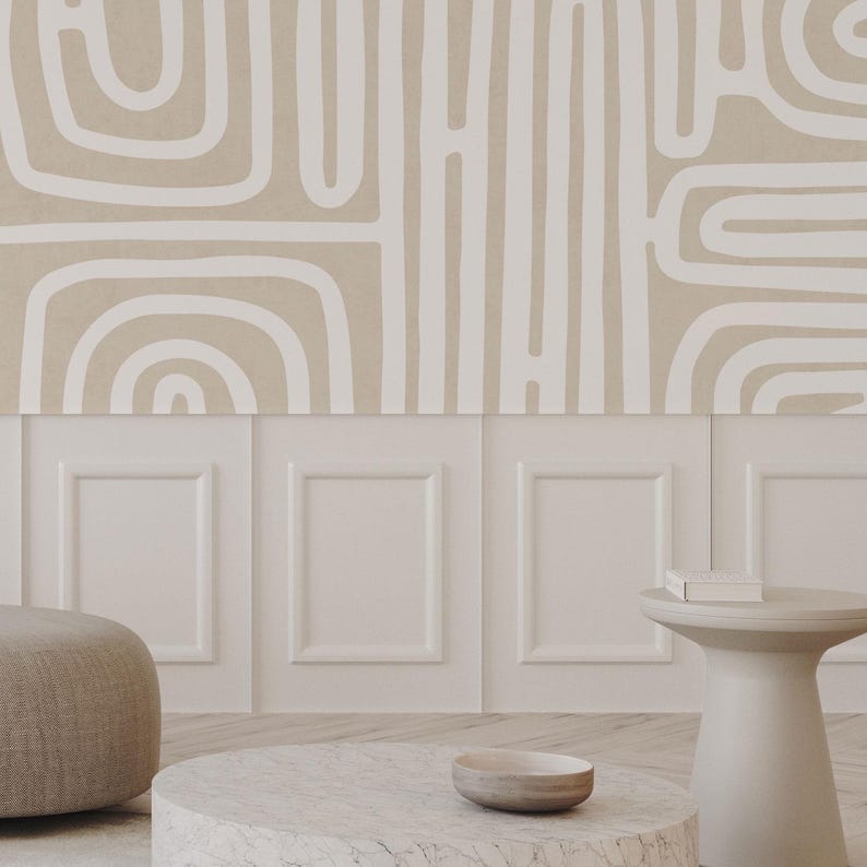 May include: A neutral-toned interior design scene featuring a beige and white abstract patterned wallpaper. Below the wallpaper is a white paneled wall. A round marble coffee table, a small side table, and a beige ottoman are in the foreground.