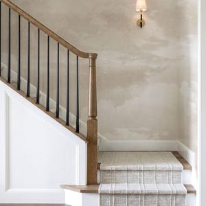 Puede incluir: Una escalera con barandilla de madera y balaustres negros. Los escalones están cubiertos con una alfombra estampada. La pared está pintada con un diseño de cielo nublado, y una lámpara de pared dorada con una pantalla blanca está montada en la pared.