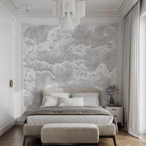 May include: A white bedroom with a bed, a white headboard, and a white bedspread. The wall behind the bed is covered in a white and gray wallpaper with a cloud design. There is a white ottoman in front of the bed.