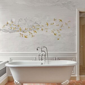 May include: A white clawfoot bathtub with ornate feet is the focal point of a bathroom. The wall features a mural of clouds and gold-colored birds. The floor is tiled in a reddish-brown hexagonal pattern. A chrome faucet and showerhead are mounted above the tub.