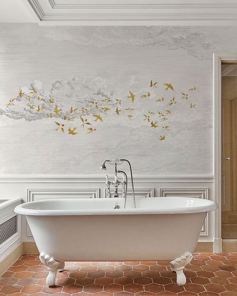 May include: A white clawfoot bathtub with ornate feet is the focal point of a bathroom. The wall features a mural of clouds and gold-colored birds. The floor is tiled in a reddish-brown hexagonal pattern. A chrome faucet and showerhead are mounted above the tub.