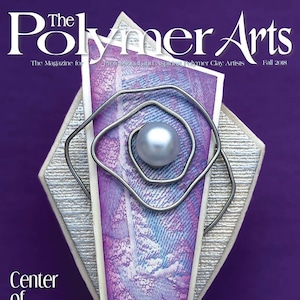 May include: The cover of Polymer Arts magazine, a magazine for polymer clay artists. The cover features a purple, white, and silver abstract design with a pearl in the center. The text "Center of Attention" is printed in black at the top of the cover.