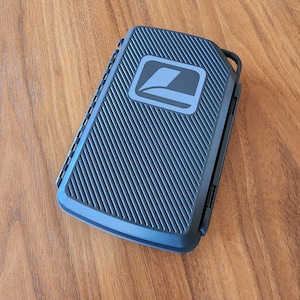 May include: A rectangular dark blue storage case with a textured diagonal ribbed surface and a smooth, rounded corner design. The center features a square logo with a stylized white graphic of a folded page or document on a dark background.