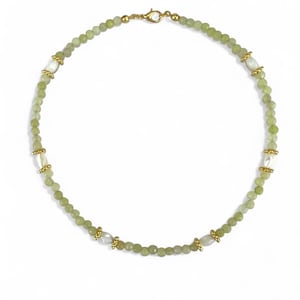 Può includere: Una delicata collana con piccole perline rotonde verde chiaro intervallate da perline bianche ovali più grandi. Accenti dorati e una chiusura dorata completano il design. La collana è presentata su uno sfondo bianco.