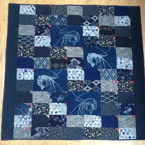 Könnte beinhalten: Eine blaue und weiße Patchwork-Decke mit geometrischem Muster. Die Decke besteht aus verschiedenen Stoffen, darunter Denim und Baumwolle. Die Decke ist mit verschiedenen Mustern verziert, darunter Wellen, Blumen und geometrische Formen.