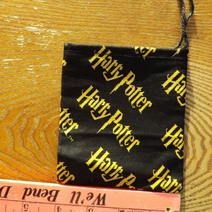 May include: A black drawstring bag with a gold "Harry Potter" print. The bag is about 4 inches wide.