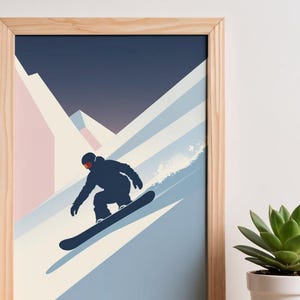 May include: A framed print featuring a snowboarder in a dark blue silhouette against a snowy mountain scene. The artwork uses a palette of blues, pinks, and white, with a dark blue sky. The frame is made of light-colored wood.
