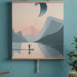 May include: A wall art print depicting a watersports scene. A person is kitesurfing on a lake, with mountains in the background. The print is framed with wooden bars and a hanging string. The color palette includes blues, pinks, and beige.