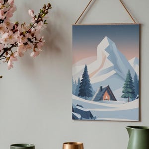 May include: A framed print showing a winter scene with a snow-covered mountain, fir trees, and a cabin with a lit fire. The artwork uses blue, white, and orange hues, and is hung by a wooden dowel and string. The print is a landscape.