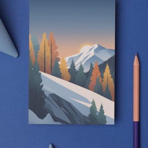 May include: A rectangular art print featuring a mountain landscape with snow-covered peaks, evergreen trees, and orange and yellow autumn trees. The artwork is set against a gradient sky with a setting sun. A blue background surrounds the print.