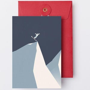 May include: Greeting card with a skier jumping off a mountain peak, set against a dark blue sky. The card is paired with a red envelope. The illustration uses shades of blue, white, and gray.