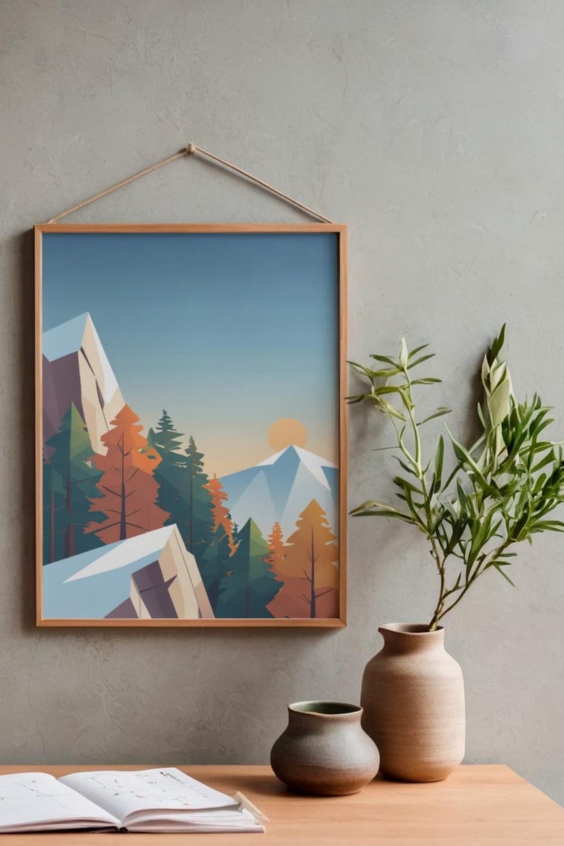 May include: A framed art print featuring a stylized mountain landscape with snow-capped peaks, evergreen and autumn-colored trees, and a setting sun. The artwork is in a wooden frame and hangs on a gray wall. A vase with greenery sits below.