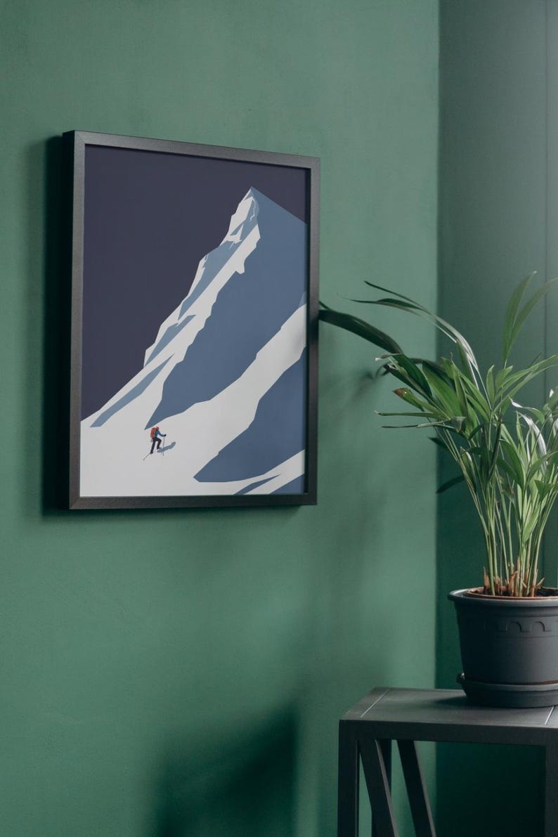 May include: Framed art print featuring a minimalist illustration of a snow-covered mountain with a skier. The artwork is in shades of blue and white, set against a dark blue sky. The print is in a black frame.