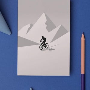 May include: A grayscale illustration of a mountain biker on a mountain trail. The cyclist is a black silhouette against a light gray background with geometric mountain shapes. A blue background with a pencil and paper accents the image.