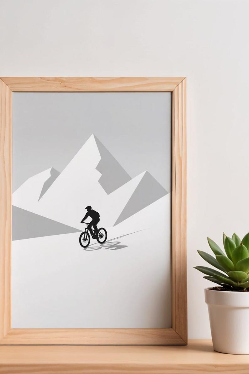 May include: Framed art print featuring a black silhouette of a mountain biker riding down a slope, set against a backdrop of stylized, geometric mountain peaks in shades of gray. The artwork is in a light wood frame.