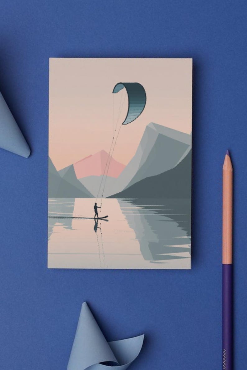 May include: A postcard featuring a watersports scene. The illustration depicts a person kitesurfing on a lake with mountains in the background. The color palette includes shades of blue, pink, and gray. A pencil and paper are on a blue surface.