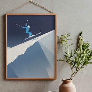 May include: A framed print depicts a skier in a blue suit and white helmet skiing down a mountain. The artwork is in a minimalist style with a dark blue sky and a light blue and white mountain. The frame is made of light brown wood.