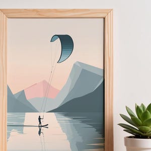 May include: A framed art print depicts a watersport scene. A person on a board is kiteboarding on a lake, with a blue and white kite overhead. Mountains in shades of blue and pink form the backdrop. The artwork is in a wooden frame.