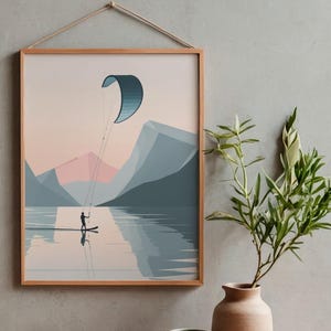May include: A framed art print depicts a watersports scene. A person on a paddleboard is kiteboarding on a lake, with mountains in the background. The artwork is in a minimalist style, with a color palette of blues, pinks, and beige.