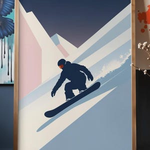 May include: A framed art print featuring a snowboarder in silhouette, carving down a snowy mountain slope. The artwork uses a palette of navy, light blue, pink, and white, with a gradient sky. The snowboarder is wearing a dark blue outfit and orange goggles.
