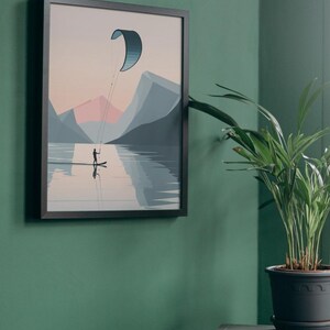 May include: Framed art print depicting a watersport scene. A person on a board is kite surfing on a lake, with mountains in the background. The artwork features a color palette of blues, pinks, and grays. The framed print is displayed on a green wall.