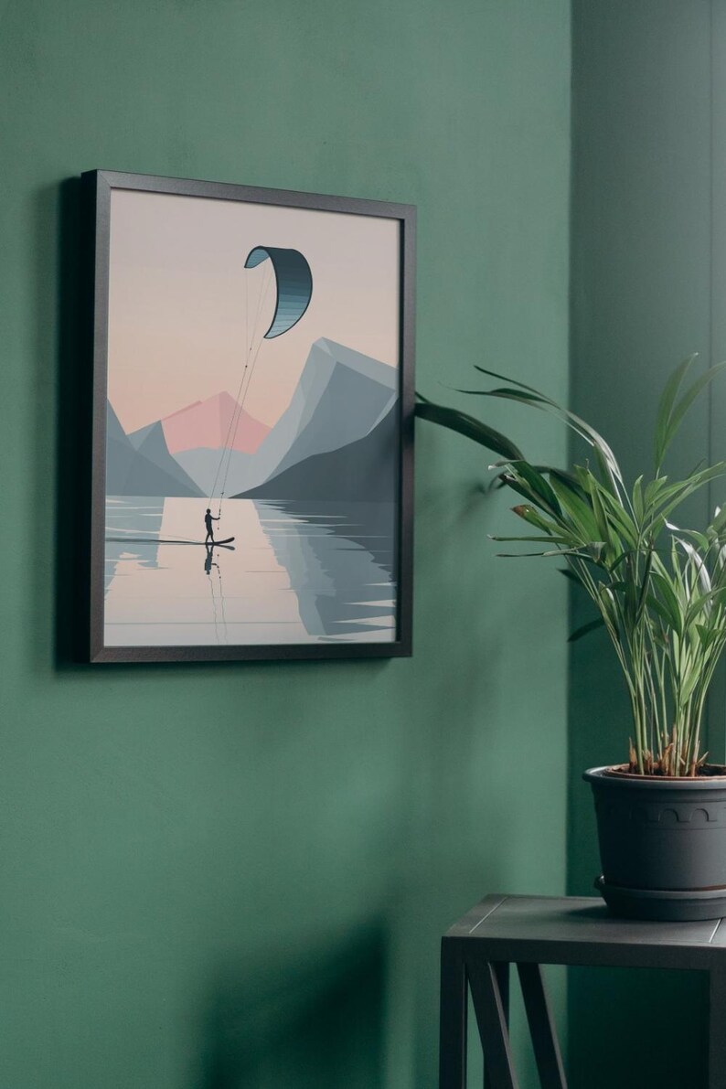 May include: Framed art print depicting a watersport scene. A person on a board is kite surfing on a lake, with mountains in the background. The artwork features a color palette of blues, pinks, and grays. The framed print is displayed on a green wall.