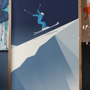 May include: Framed art print featuring a skier in a blue jumpsuit and white helmet, mid-air on skis. The artwork uses a minimalist style with a gradient blue mountain and dark blue sky. The frame is a light brown color.