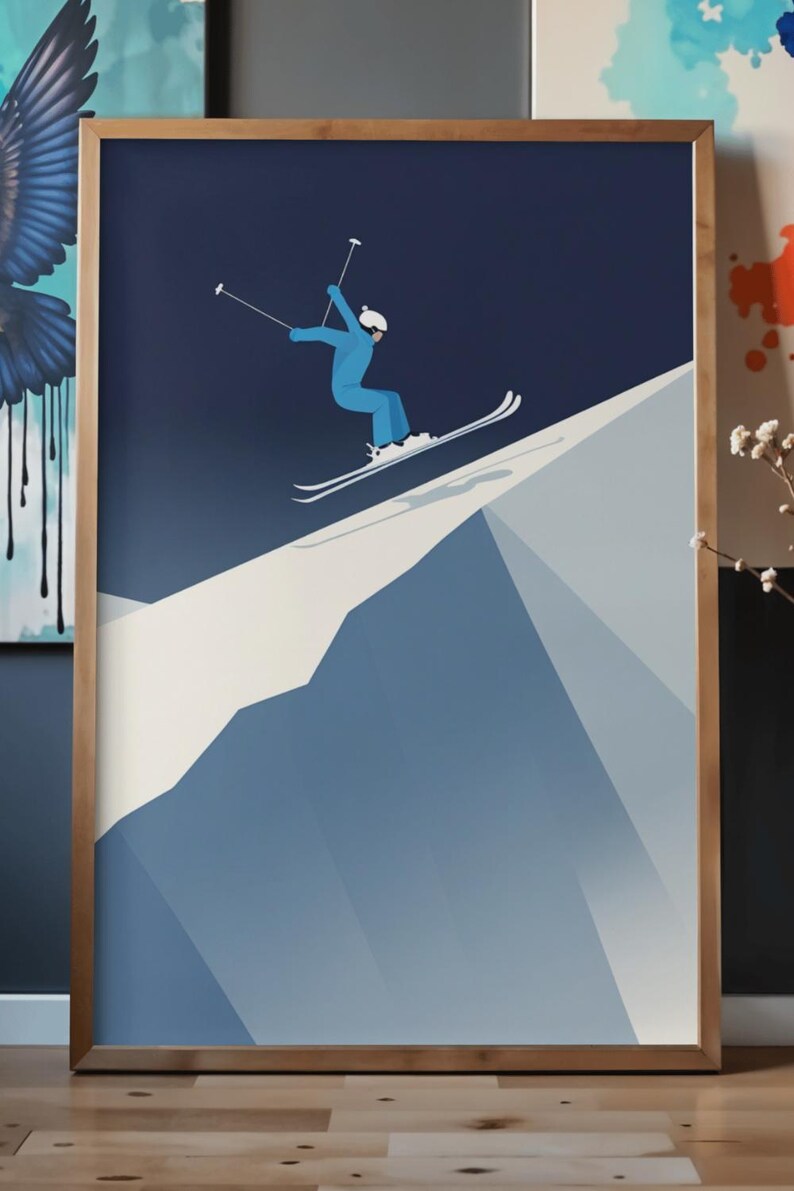 May include: Framed art print featuring a skier in a blue jumpsuit and white helmet, mid-air on skis. The artwork uses a minimalist style with a gradient blue mountain and dark blue sky. The frame is a light brown color.