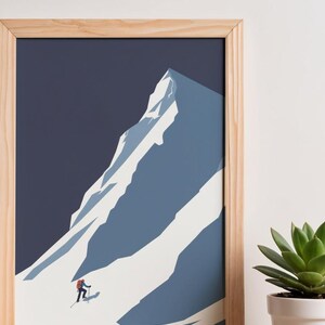May include: A framed art print featuring a minimalist illustration of a snow-covered mountain. A skier in red is ascending the slope. The artwork is set against a dark blue sky, framed in natural wood. A succulent plant in a white pot is in the background.