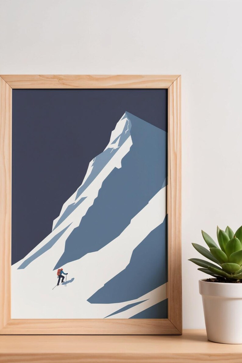 May include: A framed art print featuring a minimalist illustration of a snow-covered mountain. A skier in red is ascending the slope. The artwork is set against a dark blue sky, framed in natural wood. A succulent plant in a white pot is in the background.