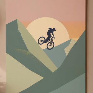May include: A mountain biking art print featuring a silhouette of a cyclist mid-air against a sunset backdrop. The artwork uses a palette of muted greens, blues, and oranges, with a large sun shape. The print is mounted on a neutral-toned background.