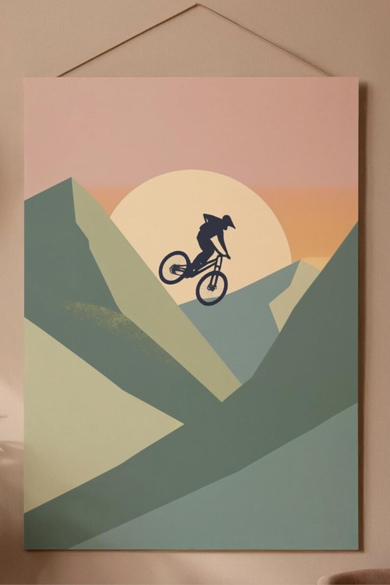 May include: A mountain biking art print featuring a silhouette of a cyclist mid-air against a sunset backdrop. The artwork uses a palette of muted greens, blues, and oranges, with a large sun shape. The print is mounted on a neutral-toned background.