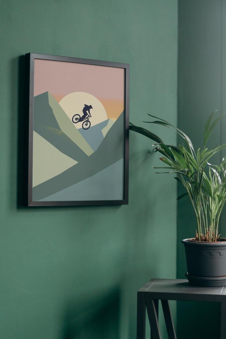 May include: Framed wall art featuring a silhouette of a mountain biker against a sunset backdrop. The artwork uses a palette of muted greens, blues, and oranges. The black frame complements the artwork, creating a modern aesthetic. Perfect for home decor.