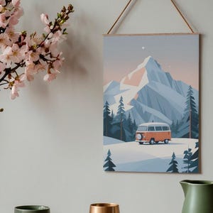 May include: A wall art print depicting a winter landscape with a mountain, pine trees, and an orange van. The artwork is displayed on a wooden frame and hung by a brown string. A green mug, a gold vase, and a green pitcher are in the foreground.