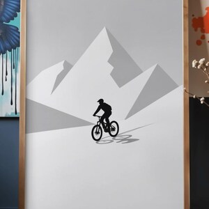 May include: A framed print featuring a minimalist illustration of a mountain biker silhouetted against a backdrop of stylized mountain peaks. The artwork is primarily in shades of gray and white, with a wooden frame.