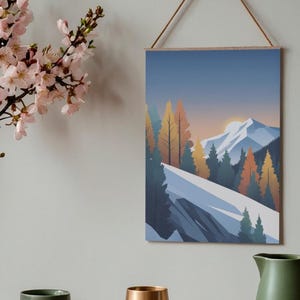 May include: A framed wall art print featuring a mountain landscape with snow-capped peaks, evergreen and autumn-colored trees, and a sunset. The print is suspended by a wooden dowel and a natural cord. A green mug, a gold-colored vase, and a green pitcher are on a wooden surface.