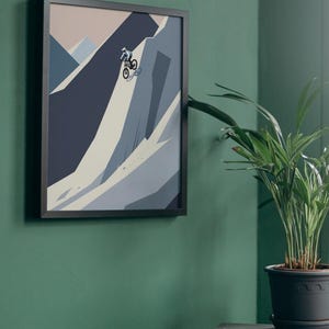 May include: Framed art print featuring a mountain biking scene. The artwork depicts a cyclist navigating a steep, rocky terrain rendered in shades of blue, gray, and beige. The print is encased in a black frame and mounted on a green wall.