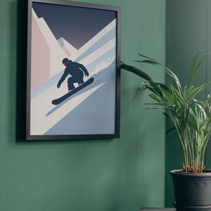 May include: Framed art print featuring a snowboarder in silhouette, descending a snowy slope. The artwork uses a minimalist style with shades of blue, white, and pink against a dark blue sky. The framed print is displayed on a green wall.