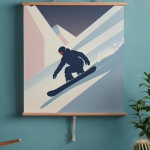 May include: A framed wall art print featuring a snowboarder in a dark blue silhouette, carving down a snowy slope. The background shows a mountain range in shades of blue, white, and pink. The print is held by wooden bars and a rope.