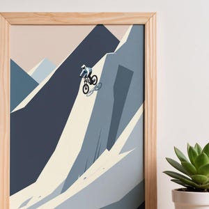 May include: A framed print featuring a mountain biker descending a steep, rocky slope. The artwork uses a minimalist style with shades of blue, gray, and beige. The print is in a natural wood frame, and a succulent plant in a white pot is in the foreground.