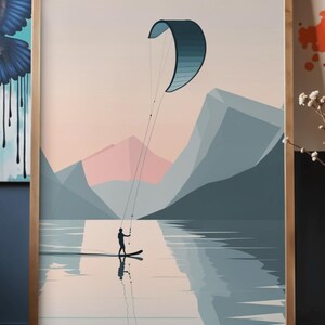 May include: Framed art print featuring a watersports scene. A person is kitesurfing on a lake, with a blue and teal kite against a backdrop of mountains and a pastel sky. The artwork is in a wooden frame.