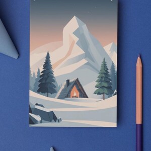 May include: A postcard depicting a winter scene with a snow-covered mountain and fir trees. A cabin with a lit fireplace is in the snow. The postcard is on a blue surface with a pencil and paper cutouts.