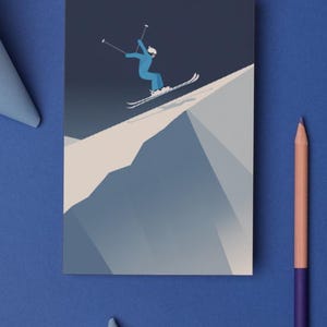 May include: A greeting card featuring a skier in a blue outfit, skiing down a snowy mountain. The illustration is set against a dark blue background. A blue pencil and paper are on the blue surface.
