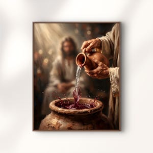 May include: A framed wall art print depicting a person in light-coloured robes pouring a dark red liquid from a clay pitcher into a large, textured clay vessel. The scene features a blurred figure in the background and warm, directional lighting.
