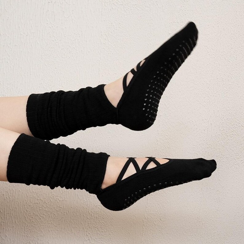 May include: Black yoga socks with crisscross straps and non-slip grips on the soles. The socks are paired with black leg warmers. The image shows the socks and leg warmers on a person's feet.